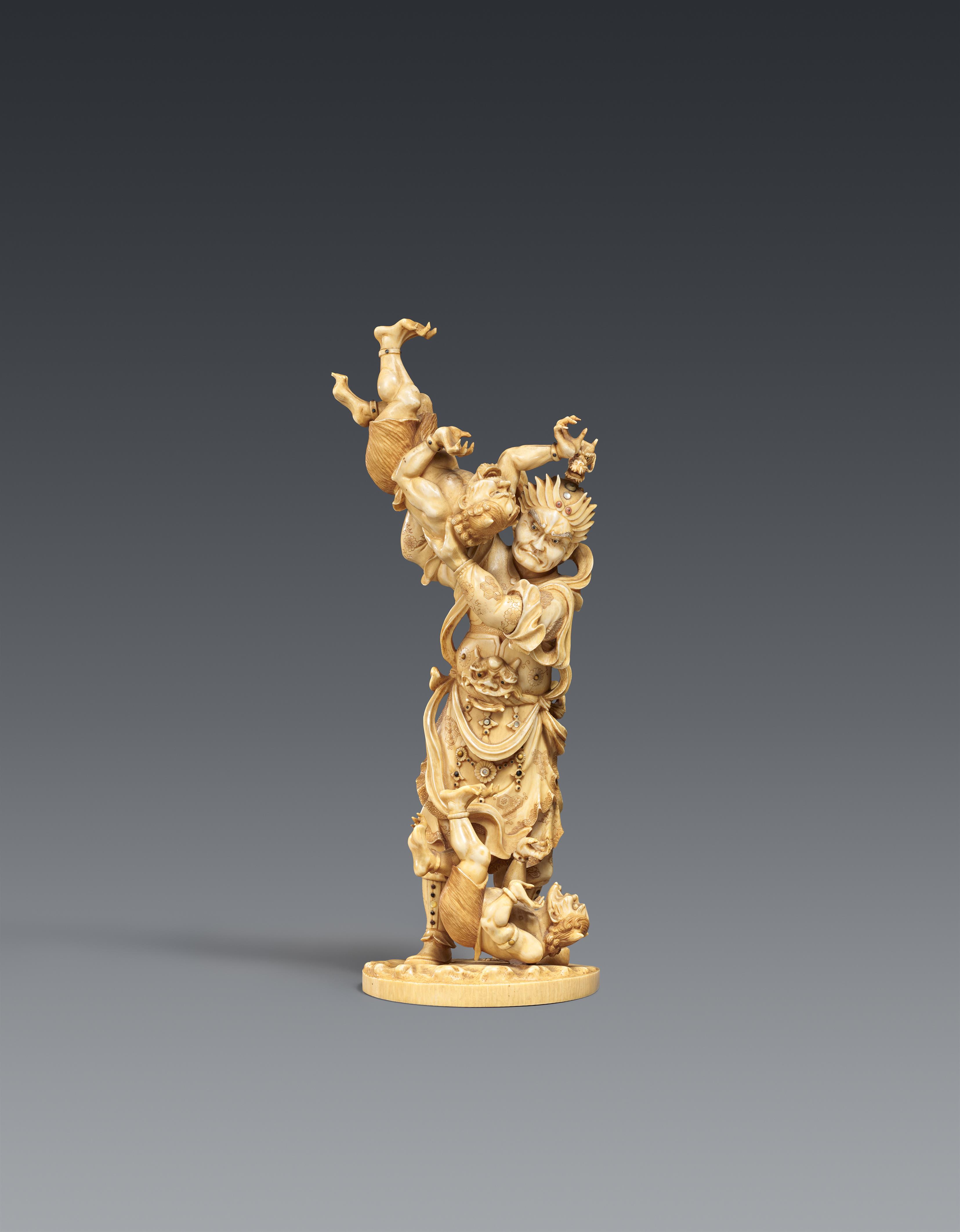 A sectional, lightly stained ivory okimono of a guardian figure with two oni. Late 19th century - image-1