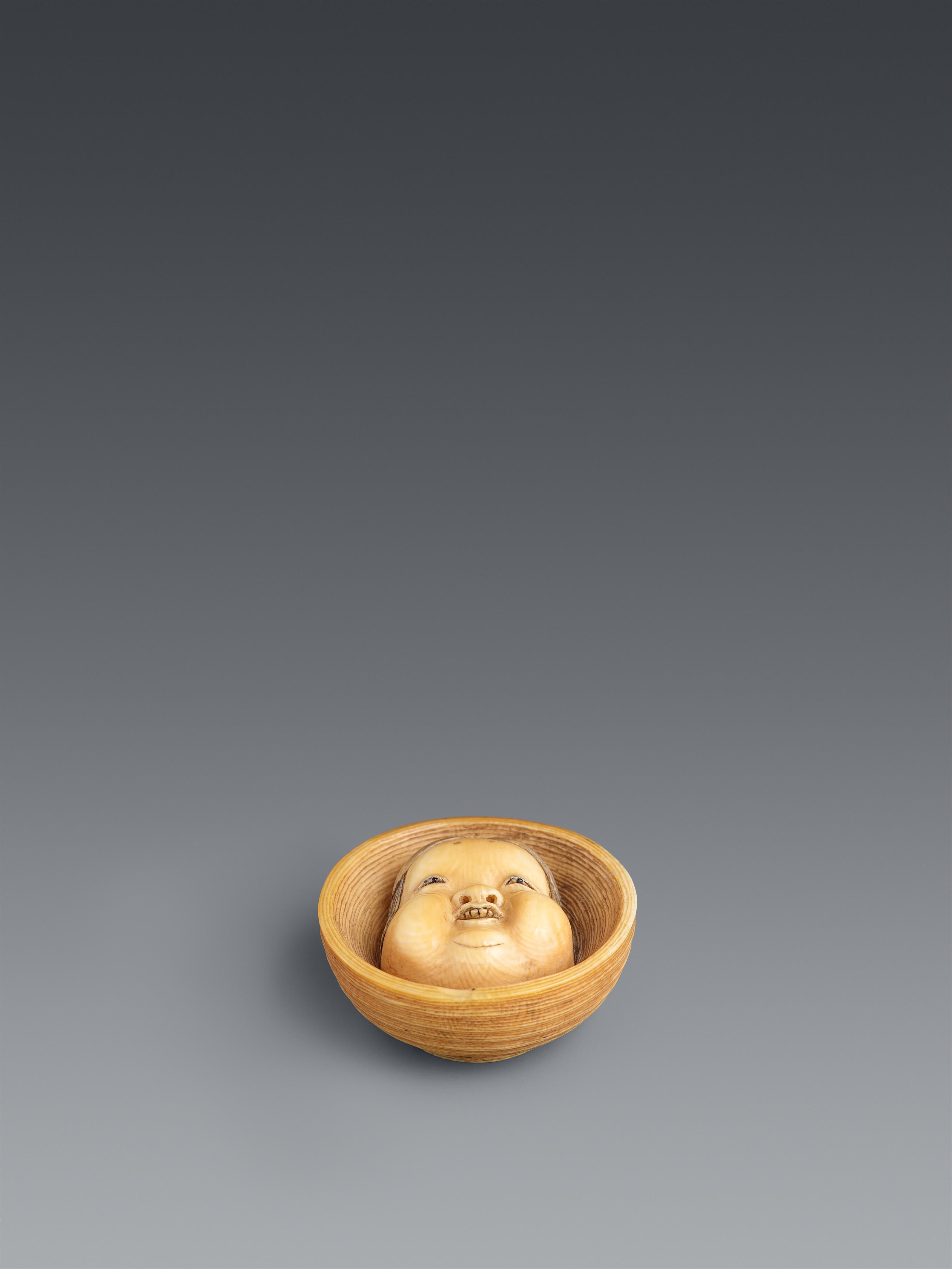 An Osaka lightly stained ivory netsuke of a Otafuku mask in a bowl. Mid-19th century - image-1