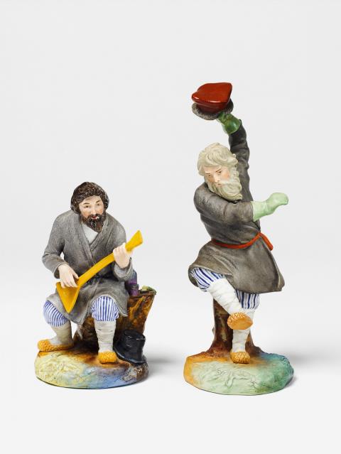  Popov - A biscuit porcelain figure of a seated peasant with a balalaika.